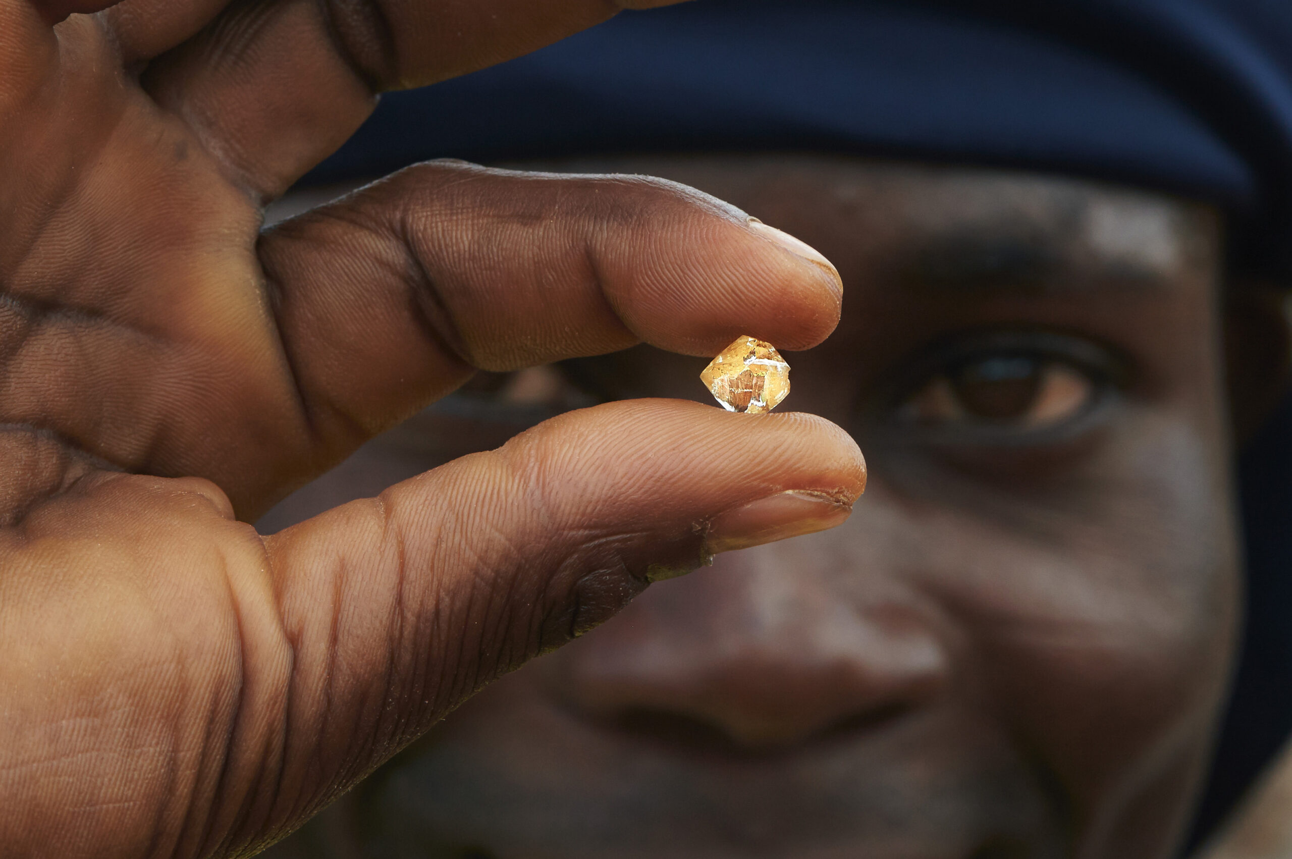 Angolan miner holding a diamond in front of his face