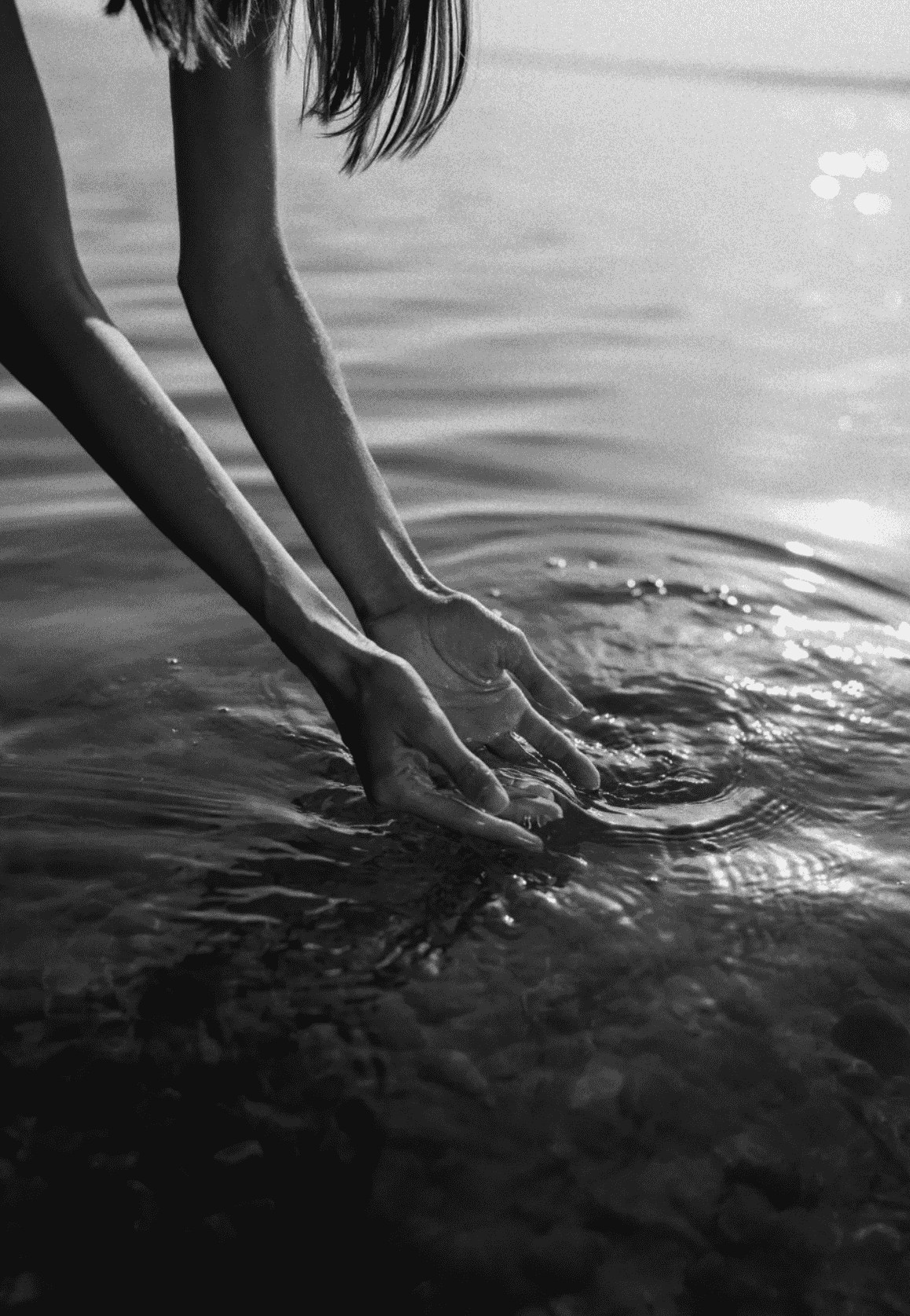 Black and white image of a woman's hands reaching into water